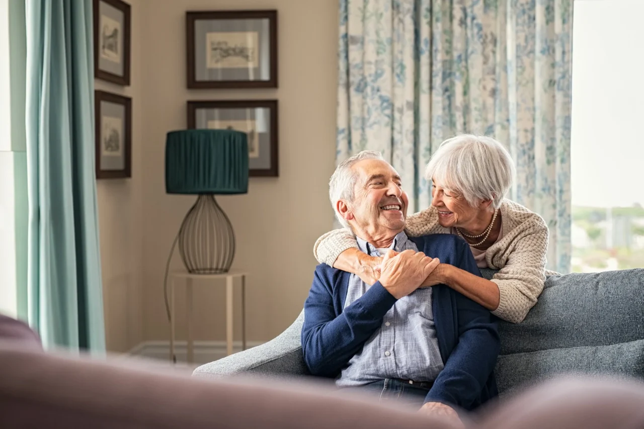 Senior couple happy smiling on couch, senior lady wrapping her arms around senior man